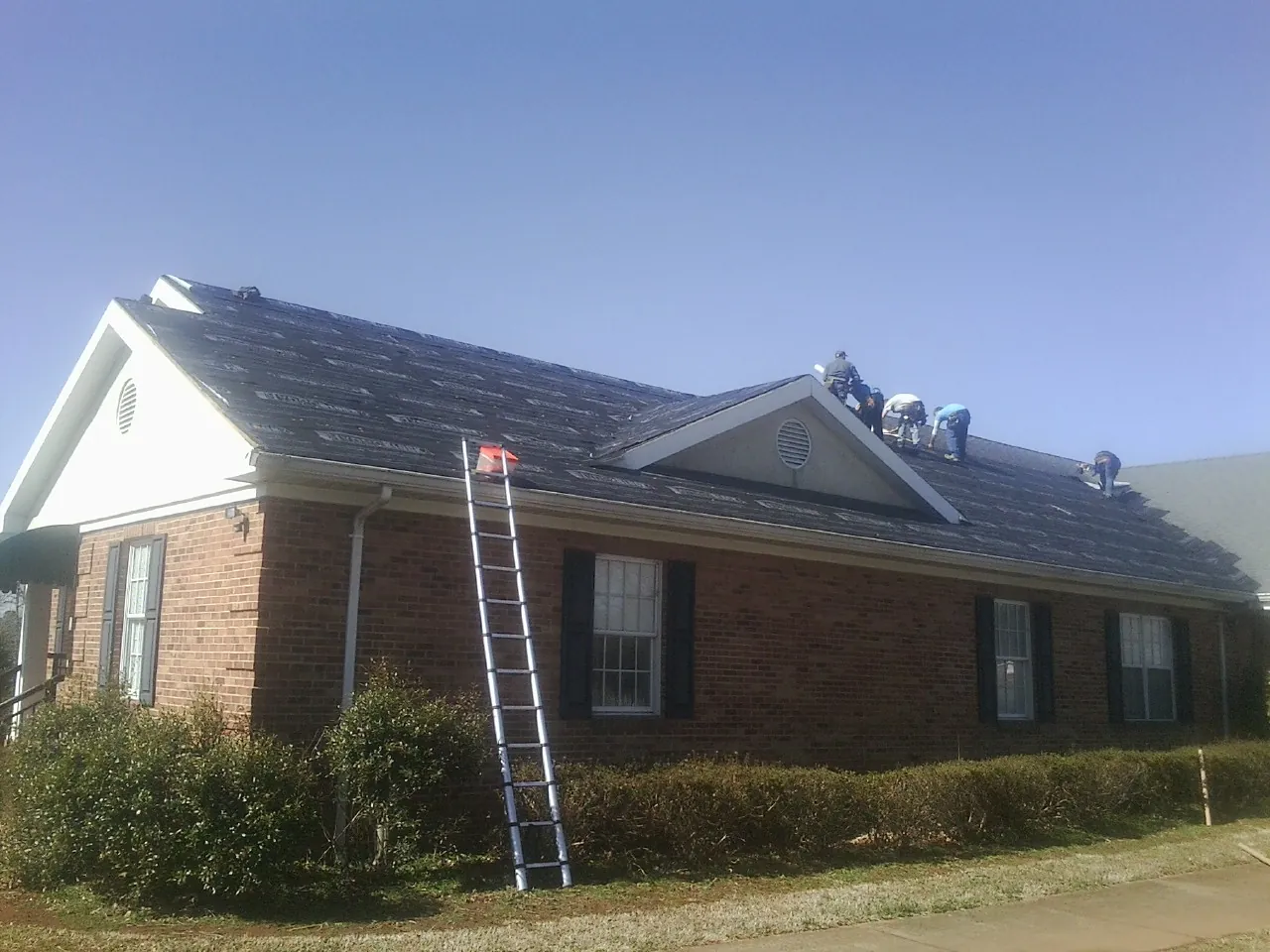 Crew tearing shingles off a brick ranch roof with a ladder set — Emergency Roof Repair work by our crew in Sardis
