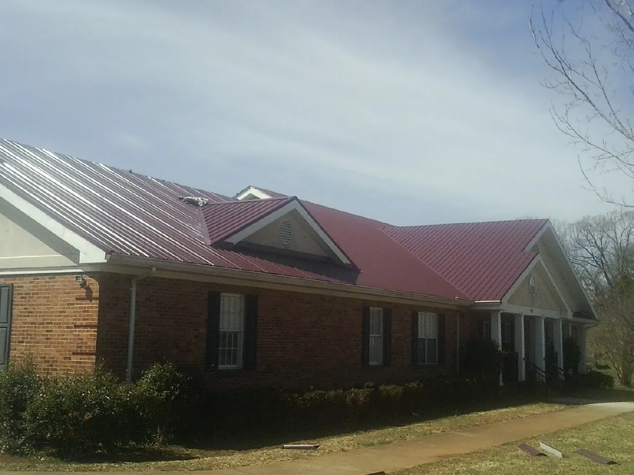 Red metal roof with gabled entries on a long brick building, from a Hail Damage Roof Repair job in Sardis