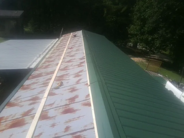 Old rusted panels beside newly installed green metal roofing — Wind Damage Roof Repair by Roofing Brothers in Sardis