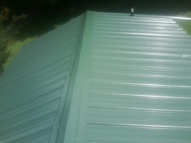 New green metal panels meeting at the ridge of a roof — Flat Roof Repair work by our crew in Sardis