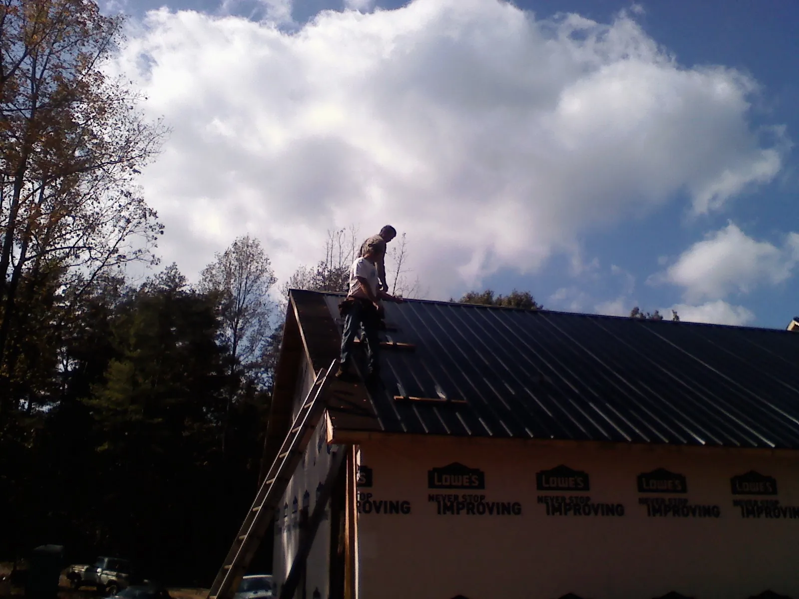 Roofer fastening dark metal panels high against a cloudy sky, from a Roof Inspection job in Sardis