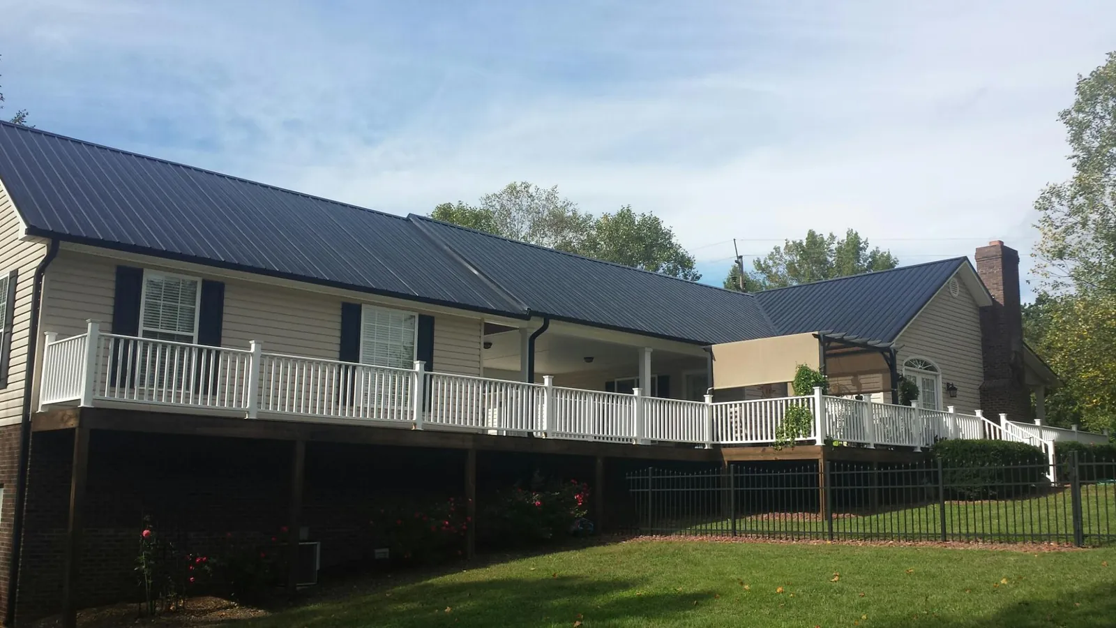 Black metal roof above a long white railed deck on a hillside home in Sardis